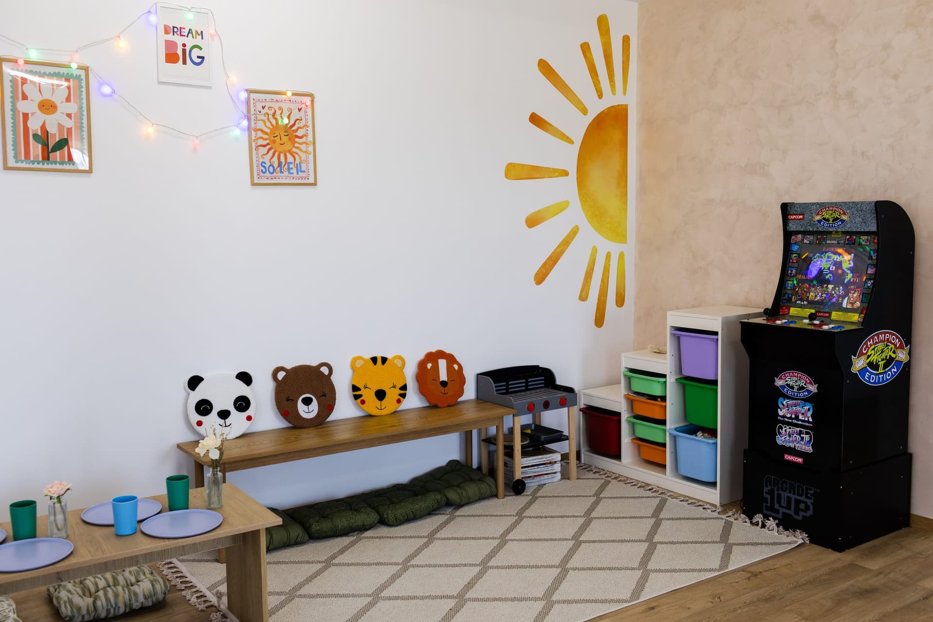 Colțul de joacă: bancă cu perne în formă de animale, cutii colorate cu jucării, grătar de jucărie și joc arcade